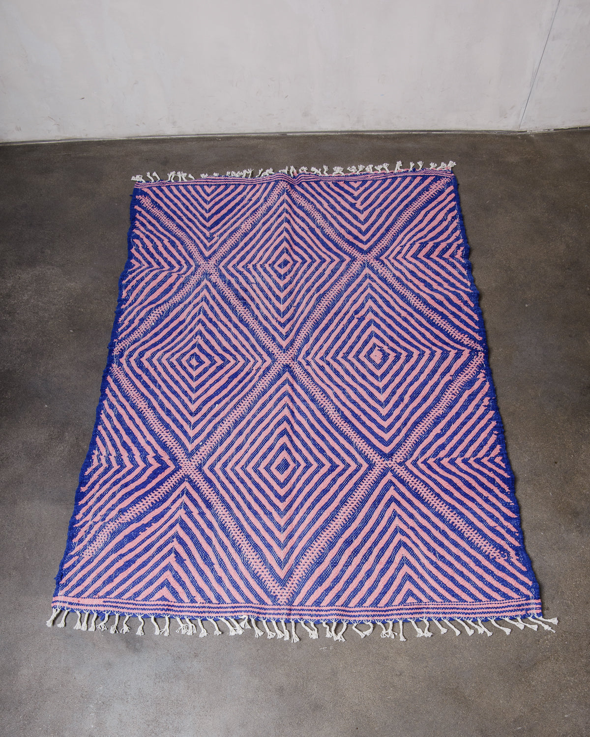 Berberlin Kelim rug made of blue and pink wool laying on concrete.